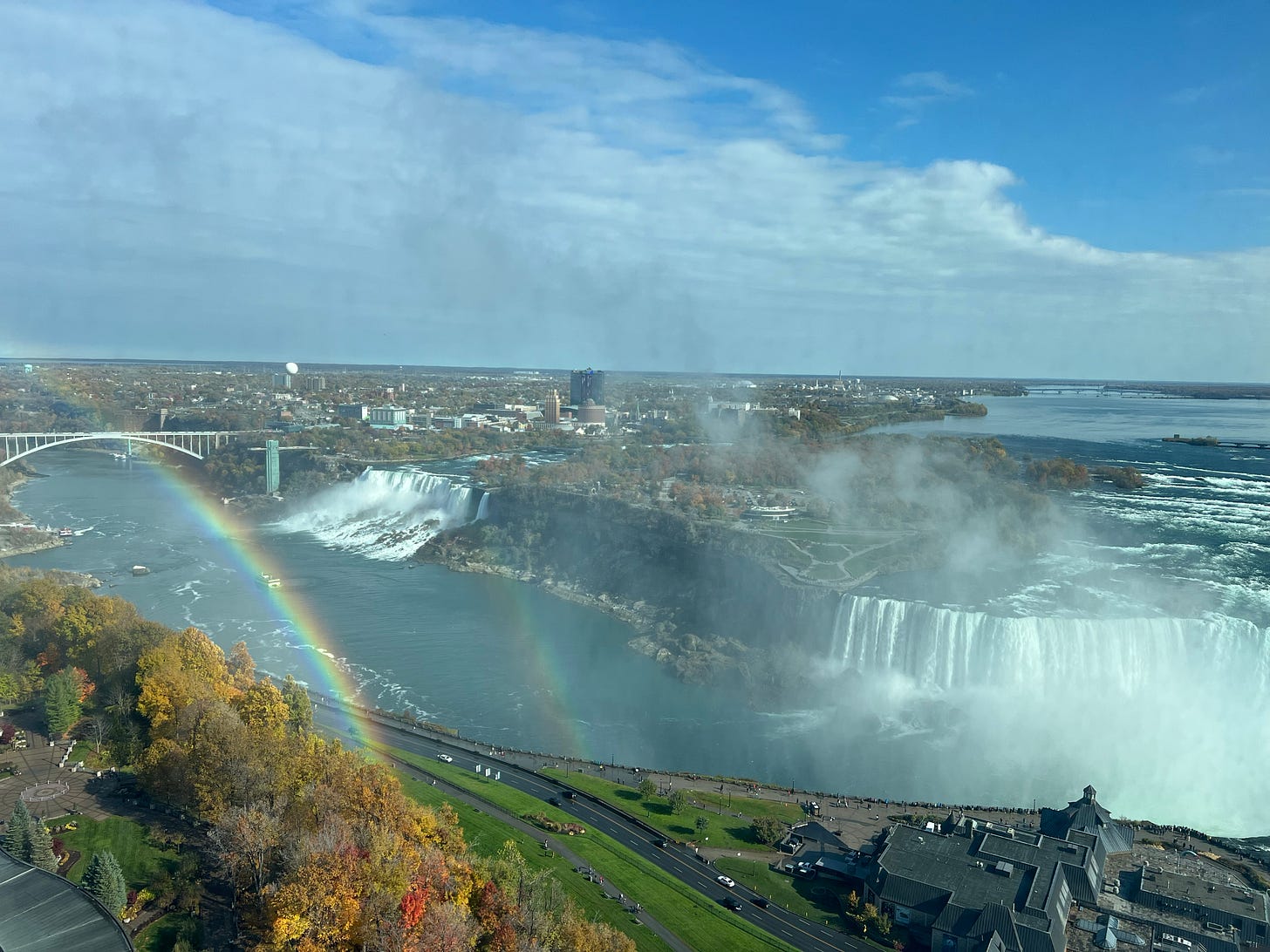 View of both Niagara Falls from 37th floor of a hotel from Canada's side, blue skies with white clouds and a double rainbow, with mostly one rainbow really visible