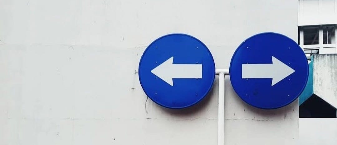 Two blue signs pointing in opposite directions on a white wall