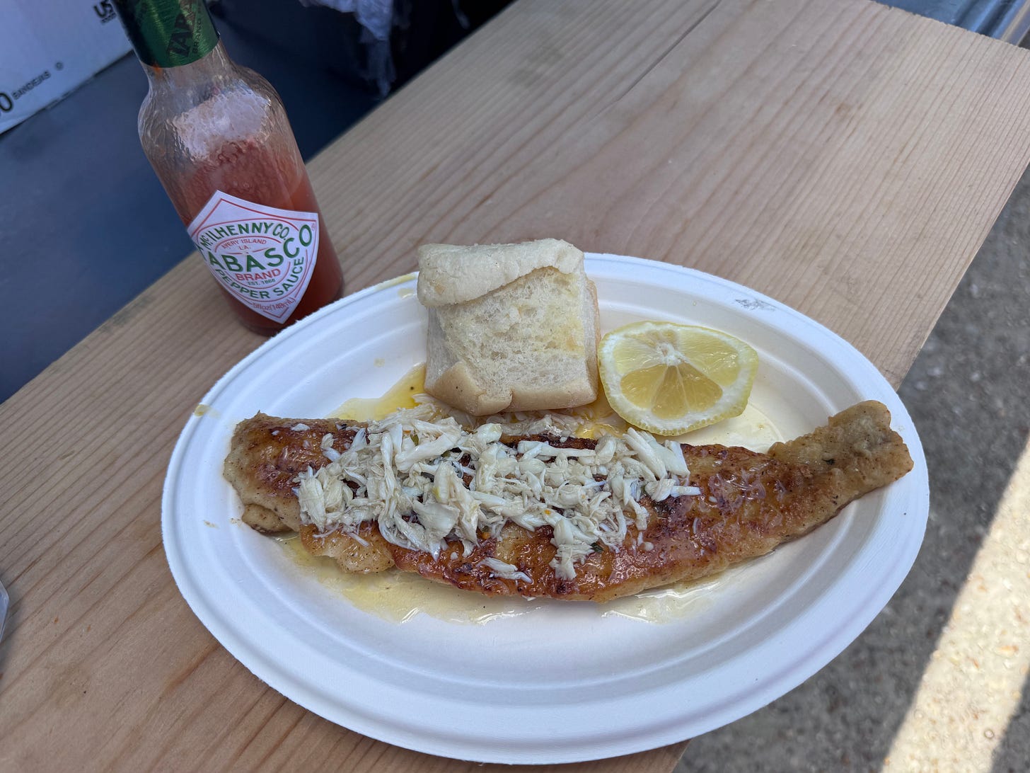 crabmeat topped grilled trout on a paper plate next to a bottle of Tabasco sauce crabmeat topped grilled trout on a paper plate next to a bottle of Tabasco sauce