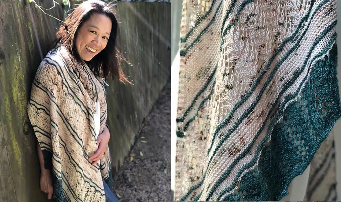 A woman stands in front of a wooden fence wearing a speckled cream and teal lace shawl. 