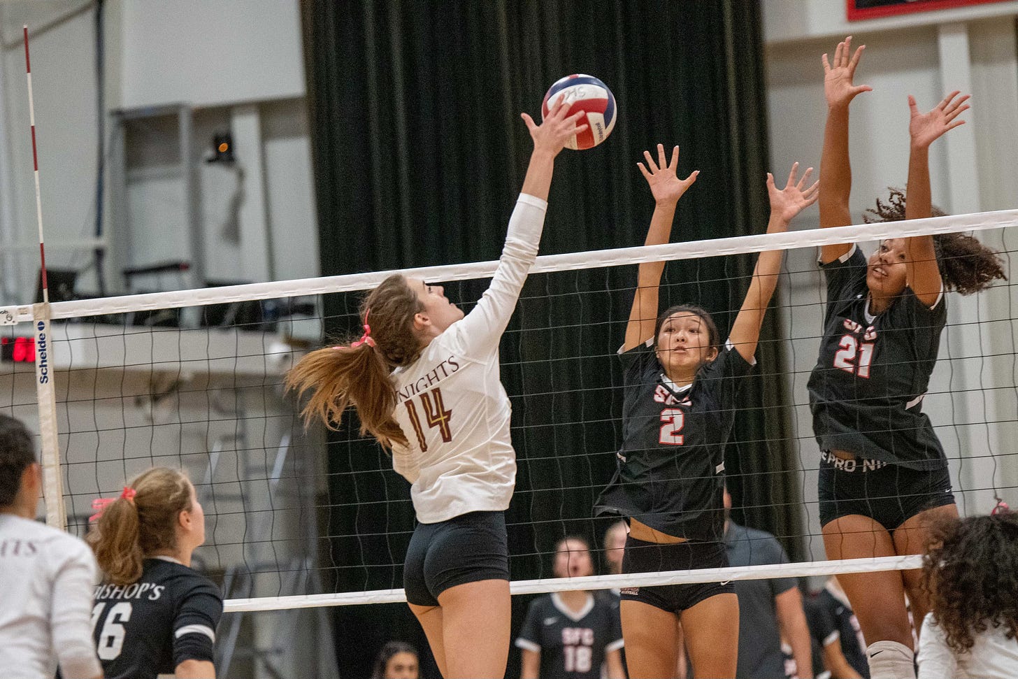 A volleyball attacker hits against two blockers