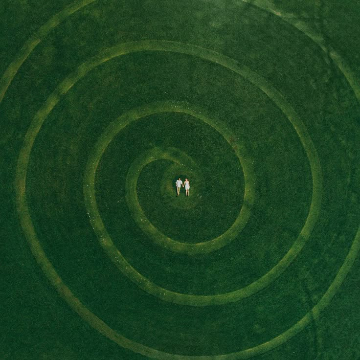 This may contain: two people are standing in the middle of a circular grass field, looking down at them