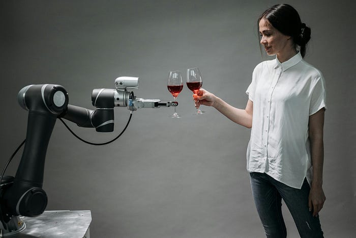 A robot arm and a woman holding glasses of wine and toasting each other