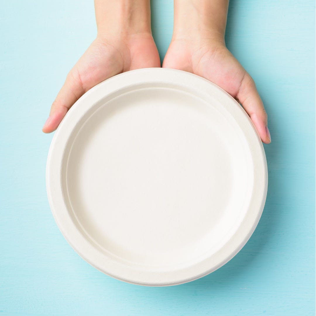 A photo of a set of pale-skinned hands holding a white plate facing up to the camera against a blue background. A photo of a set of pale-skinned hands holding a white plate facing up to the camera against a blue background.