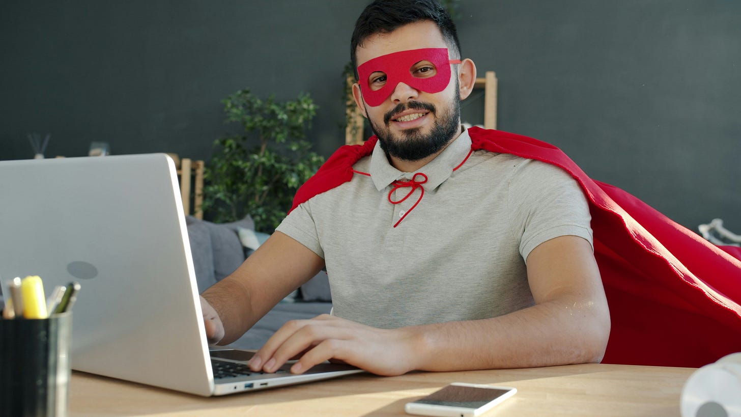 A man dressed in a superhero costume writes at his laptop