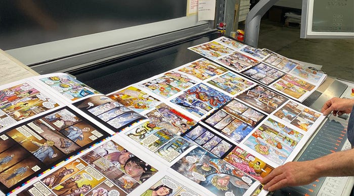A selection of printed graphic novel pages laid out across a table.