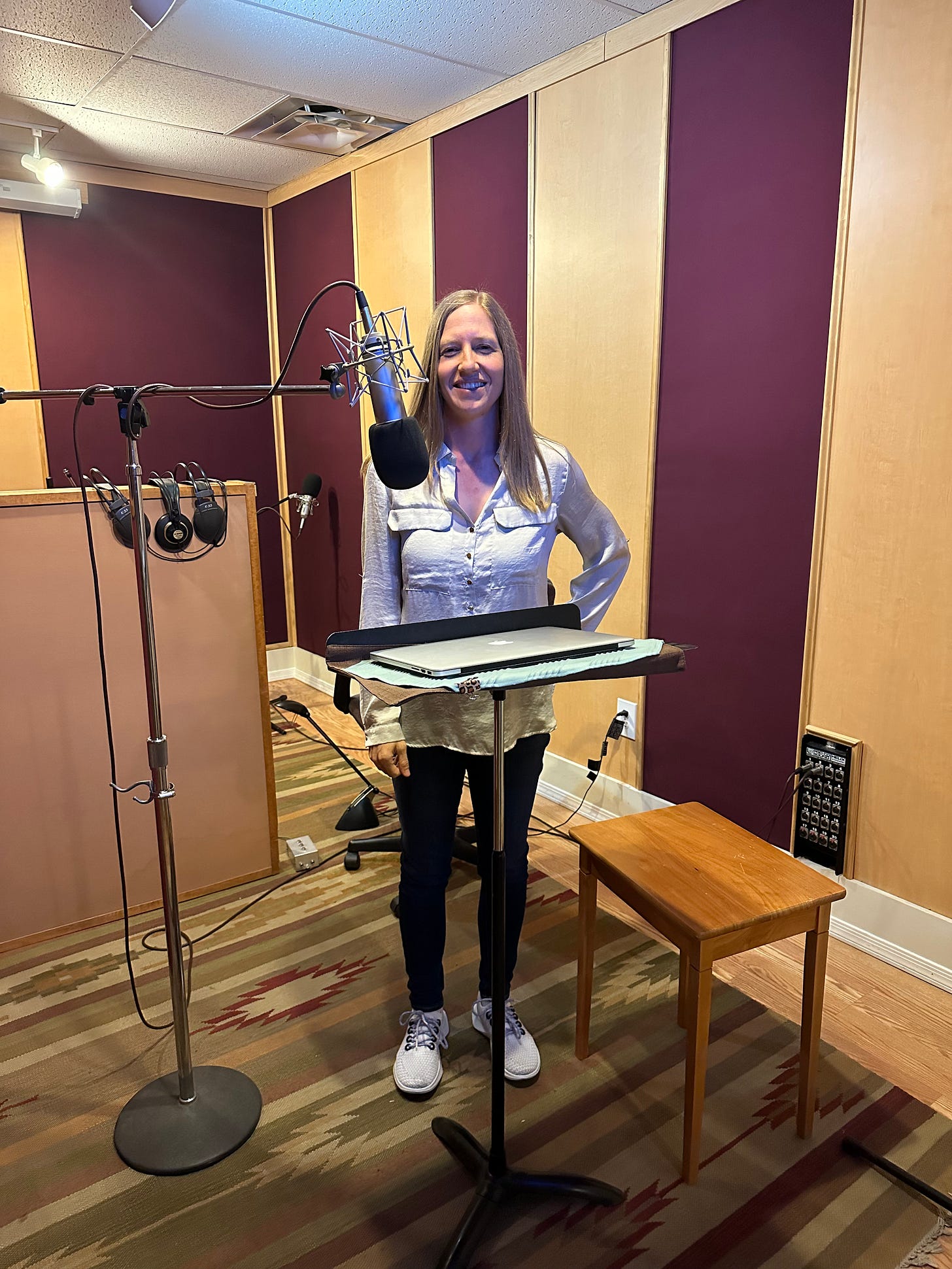 Me standing in the recording booth, grinning in front of the microphone and a music stand. I'm wearing a white shirt and jeans.