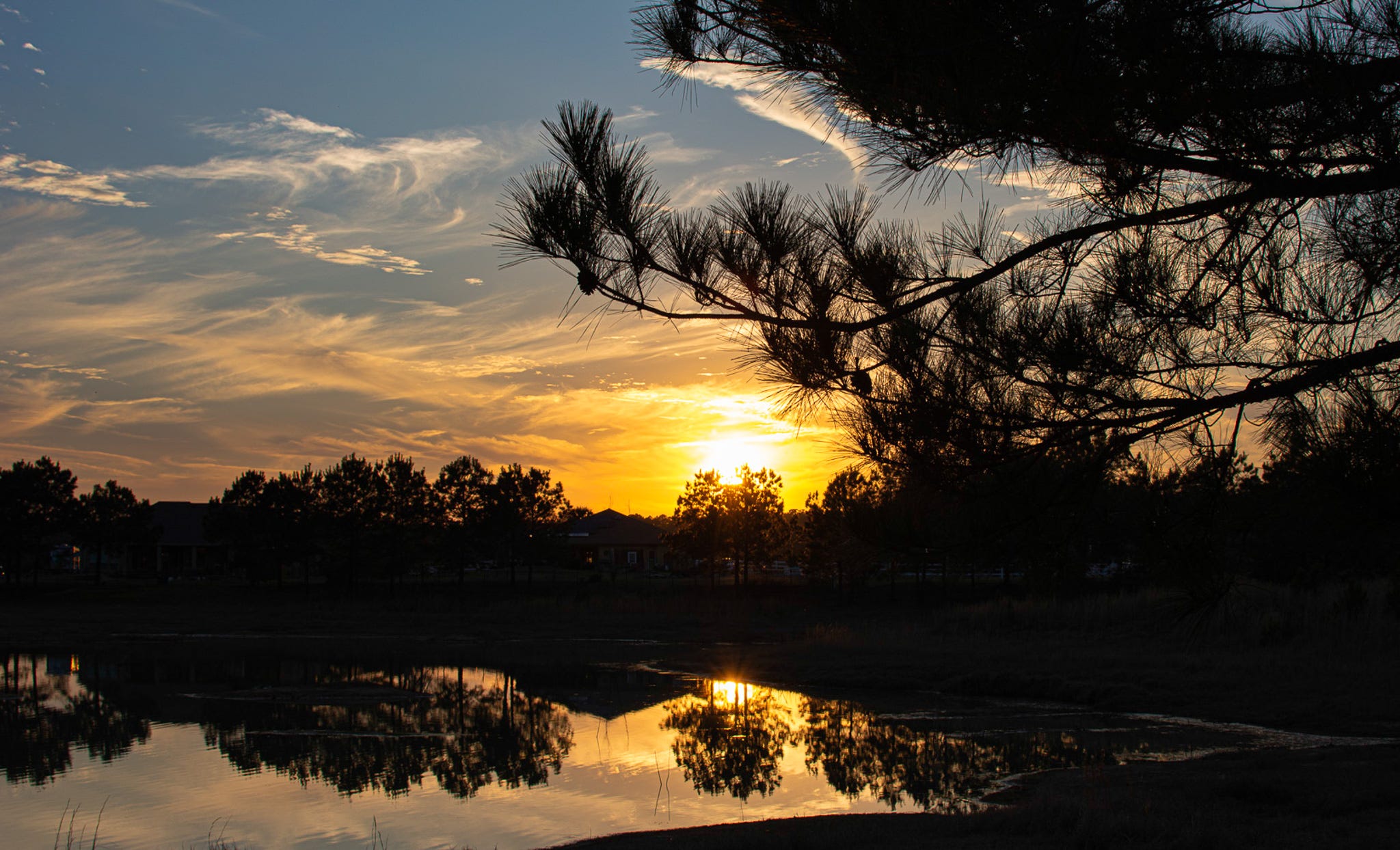 A sunset reflected in a lake; trees line the shore