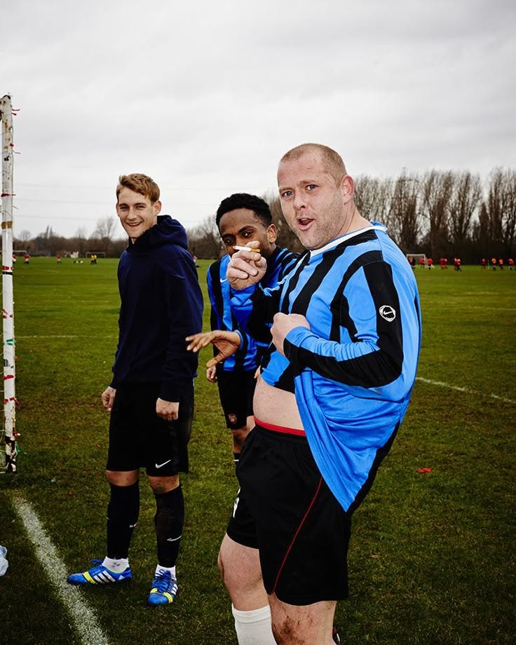 This may contain: three men standing on a soccer field posing for the camera with one man wearing a blue and black jersey