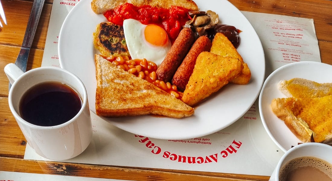 A plate of breakfast food with a tea and toast next to it A plate of breakfast food with a tea and toast next to it