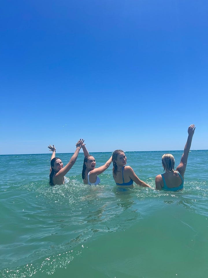 white lounge chairs with water bottle and sun glasses; girls swimming in the ocean
