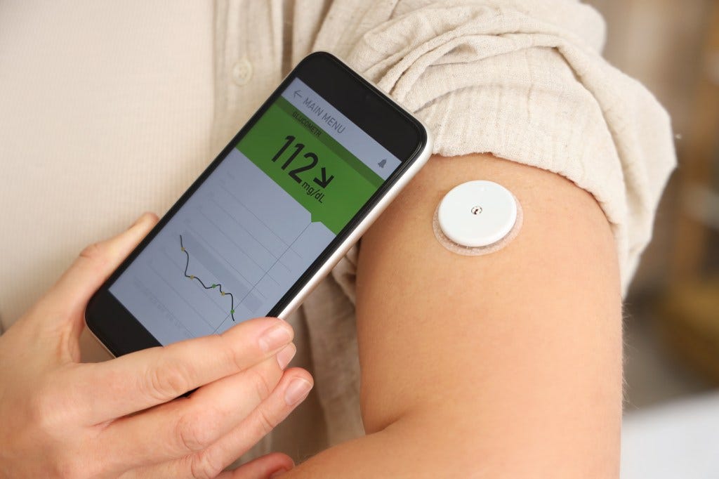 Diabetic woman with glucose sensor using mobile phone for measuring blood sugar level in bedroom