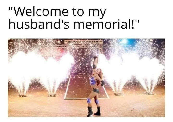 A woman in a wrestling outfit holding a championship belt, standing on a stage with white fireworks erupting around her. The text "Welcome to my husband\'s memorial!" is overlaid in white. A woman in a wrestling outfit holding a championship belt, standing on a stage with white fireworks erupting around her. The text "Welcome to my husband\'s memorial!" is overlaid in white.