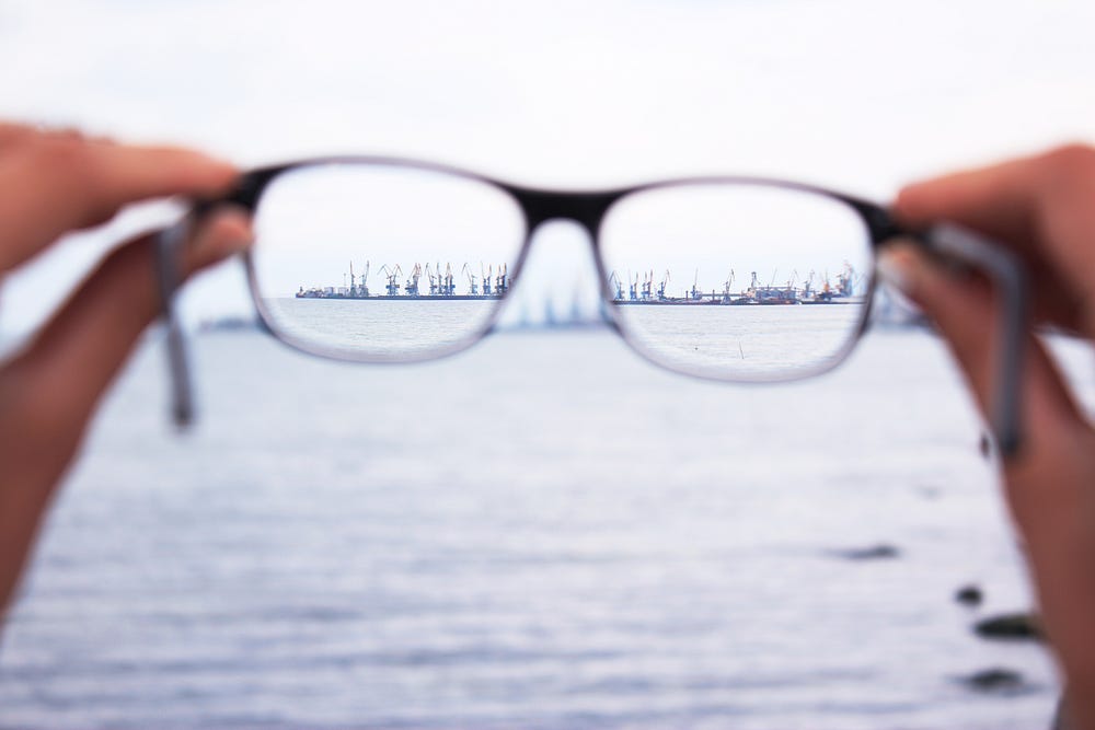 Photo of glasses being held by two hands. We look through the glasses to see a clear picture of the horizon. Photo of glasses being held by two hands. We look through the glasses to see a clear picture of the horizon.