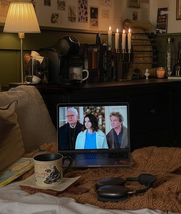 This may contain: an open laptop computer sitting on top of a bed next to a cup and book