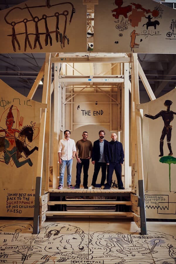 Four men stand in a row on the bottom structure of a Ferris wheel.