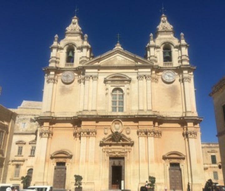 Grand, ornate building facade, two turrets, two clocks and steps to the entrance against a bright blue sky