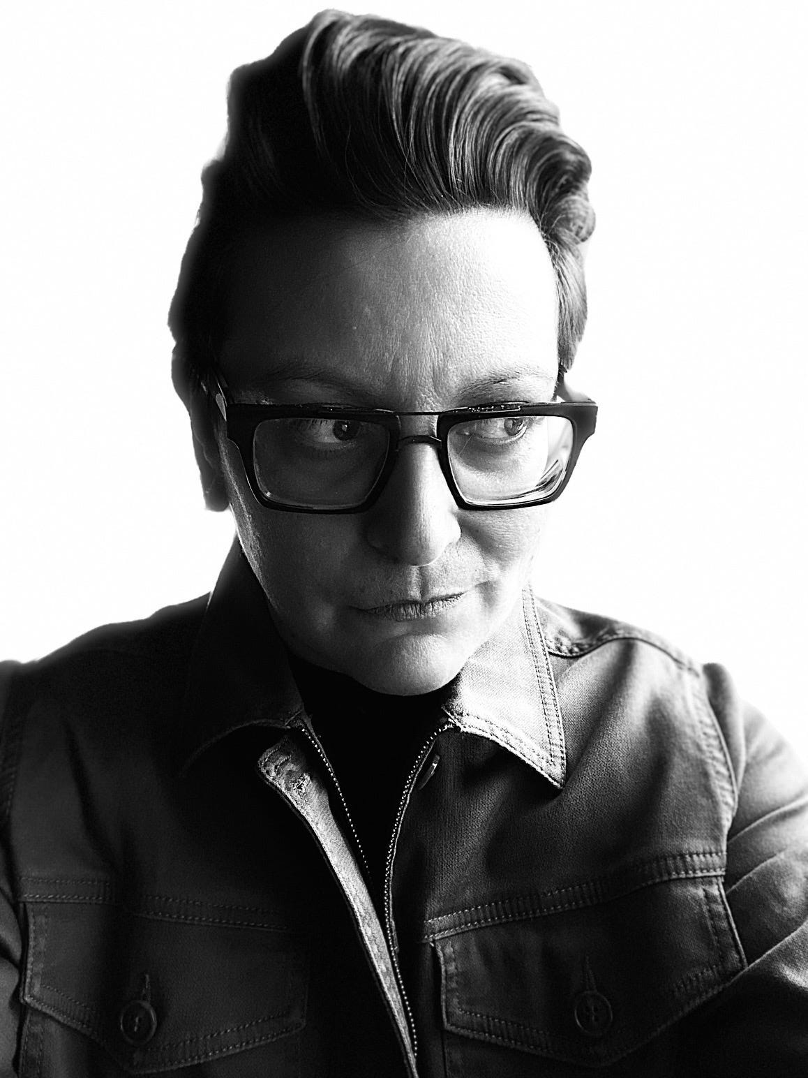 black and white headshot of Jami Smith, the creator of Songs That Saved Your Life, wearing black glasses. 