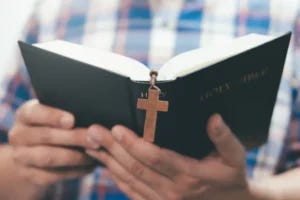 Hands holding an open Bible with crucifix bookmark