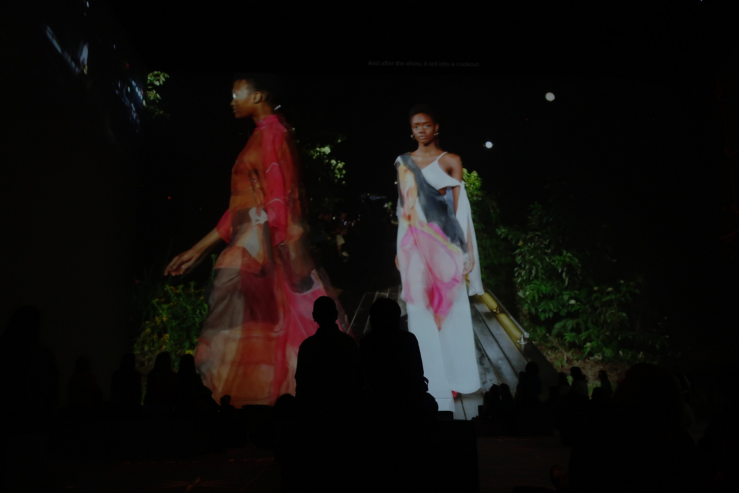 Wearing flowing dresses, two models walk in a fashion show