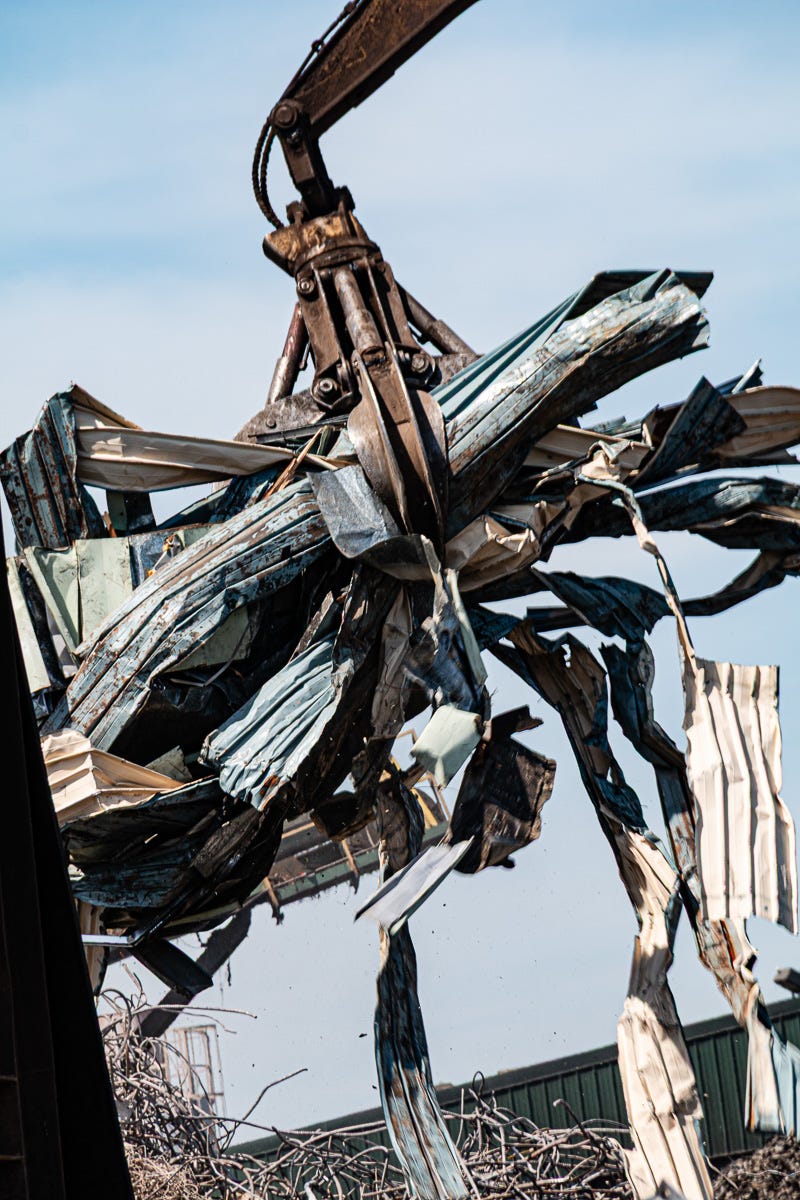Close-up of crane claw lifting a tangled bundle of bent metal and siding high into the air.