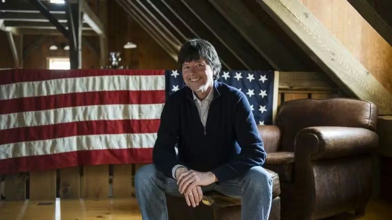 Documentarian Ken Burns sitting in front of an American flag