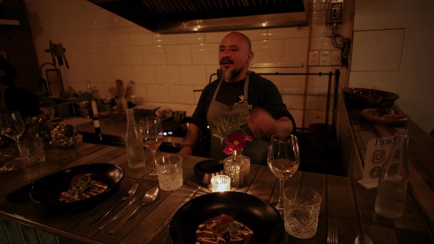 Chef-sommelier Jonas talks with guests from behind the ten-seat counter at Pipicha Santa, plated courses and candles in the foreground. Chef-sommelier Jonas talks with guests from behind the ten-seat counter at Pipicha Santa, plated courses and candles in the foreground.