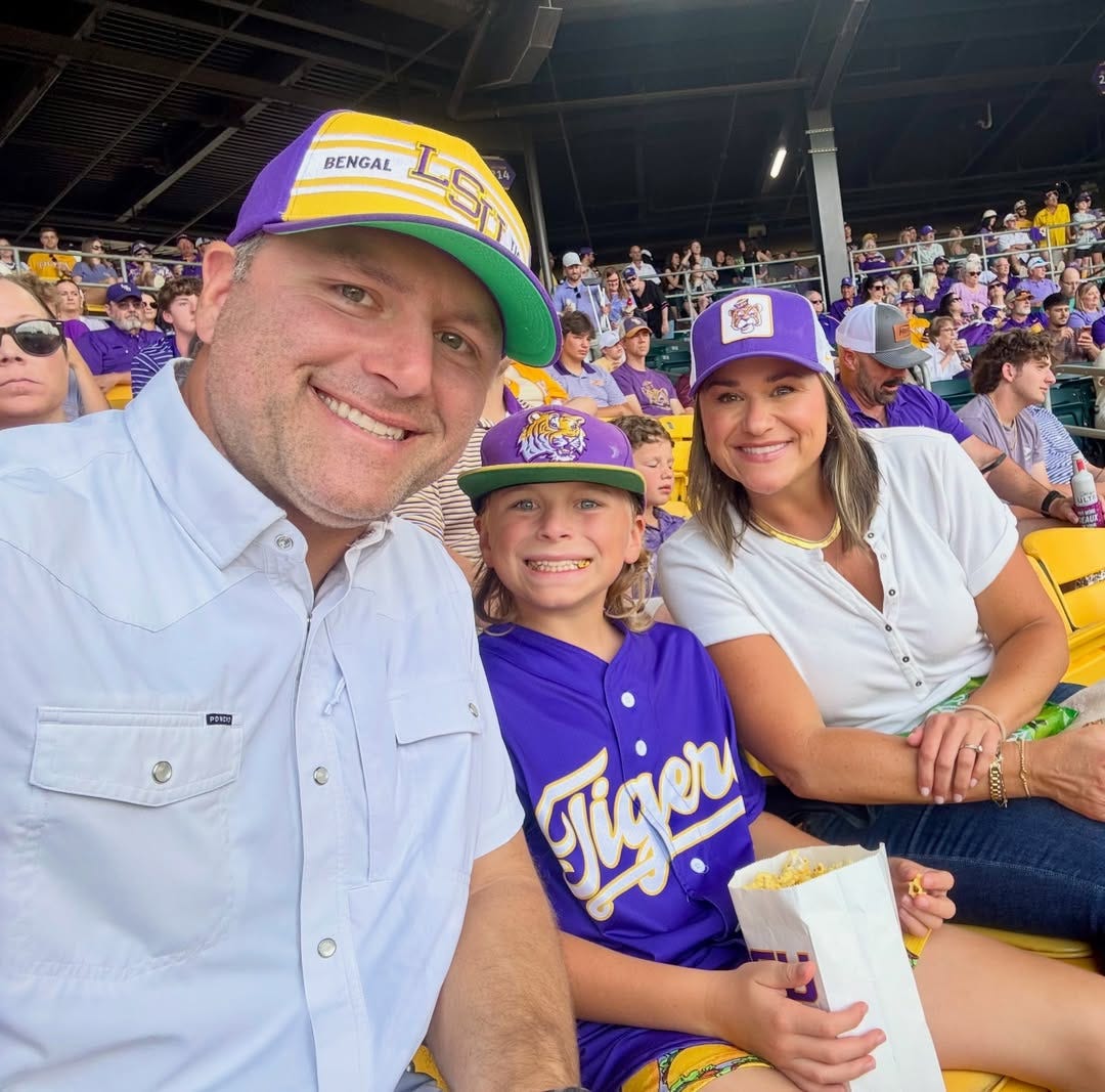 Leigh Ann, her son, and her husband at an LSU baseball game dressed in LSU purple and yellow clothing Leigh Ann, her son, and her husband at an LSU baseball game dressed in LSU purple and yellow clothing
