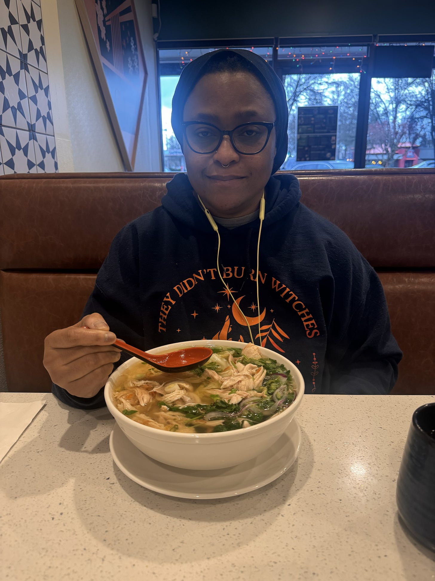 A person seated at a table with a large bowl of steaming soup, holding a spoon, conveying warmth, comfort, and quiet joy.