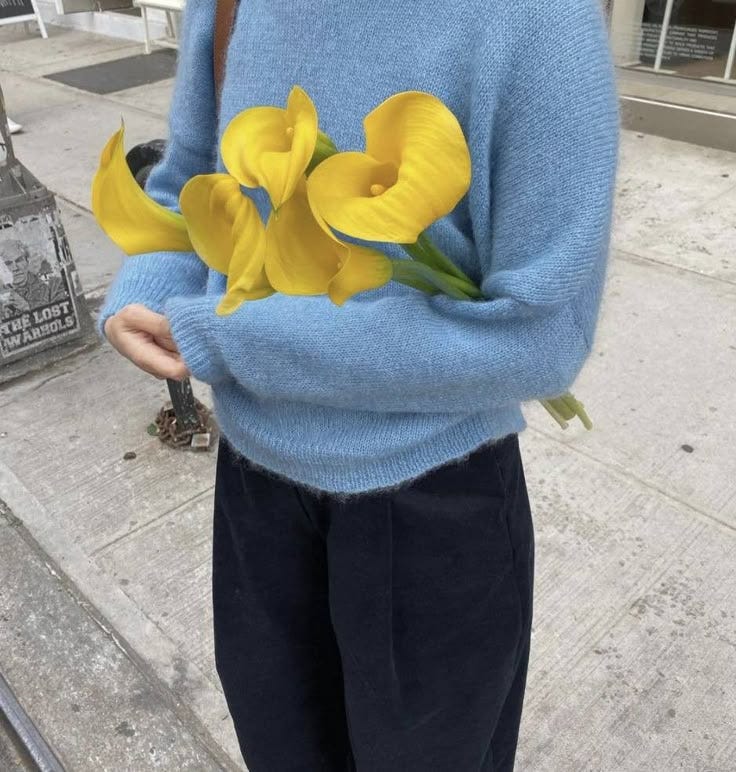 This may contain: a person wearing a blue sweater holding yellow flowers