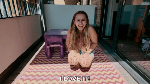 Hannah on her balcony squinting in the sunlight and saying, "I love it"