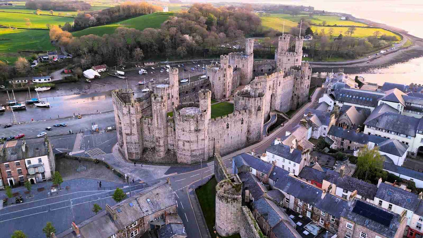 Aerial view of Caernarfon Castle in Wales — site of the 2013 NHS shingles vaccine rollout that became the cleanest natural experiment on vaccines and dementia. Aerial view of Caernarfon Castle in Wales — site of the 2013 NHS shingles vaccine rollout that became the cleanest natural experiment on vaccines and dementia.