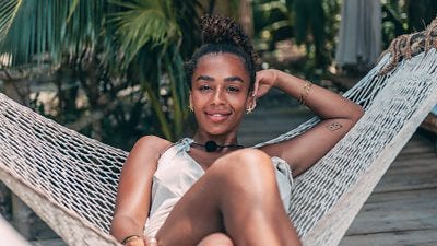 A woman sits in a hammock, smiling, resting her head on one arm