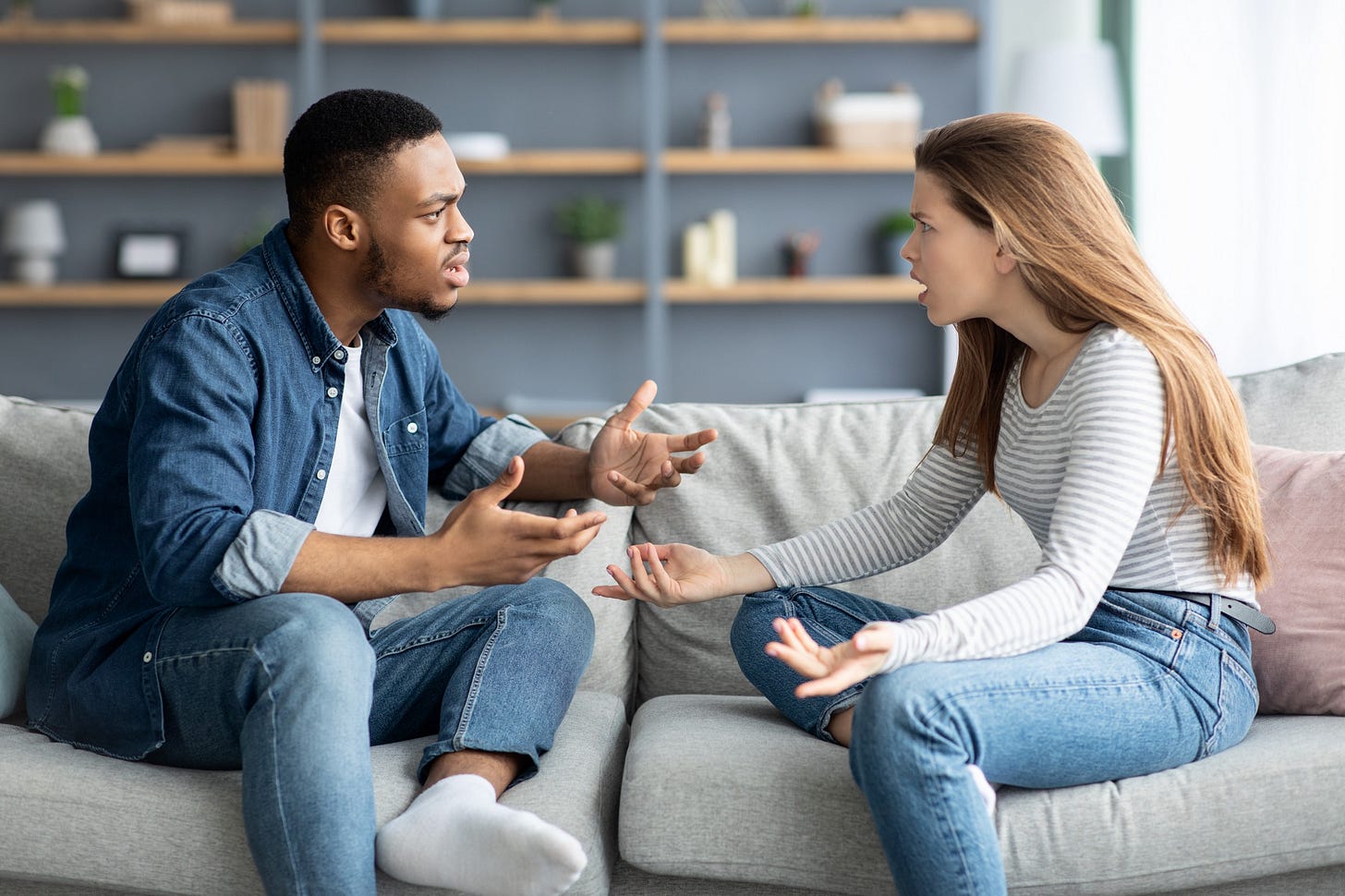 A young couple argues with one another on the sofa in their living room. A young couple argues with one another on the sofa in their living room.