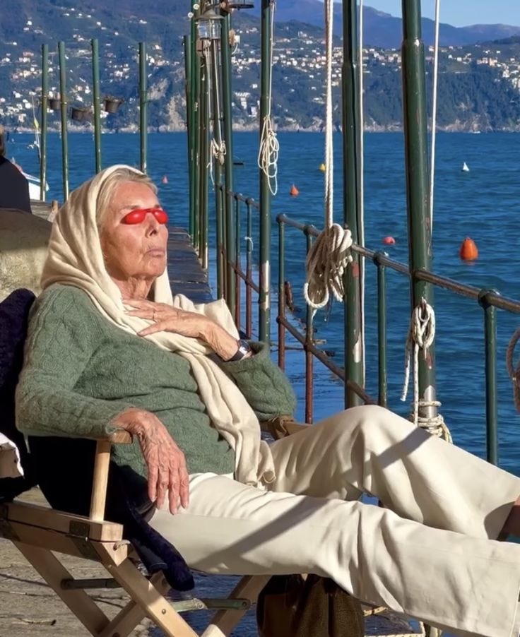 This may contain: an old woman sitting on a chair next to the water