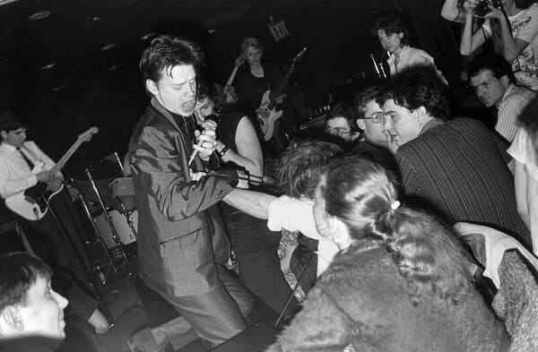 A black and white photograph of Mr. Chance, who is holding a microphone in one hand and pulling away from audience members during a performance.