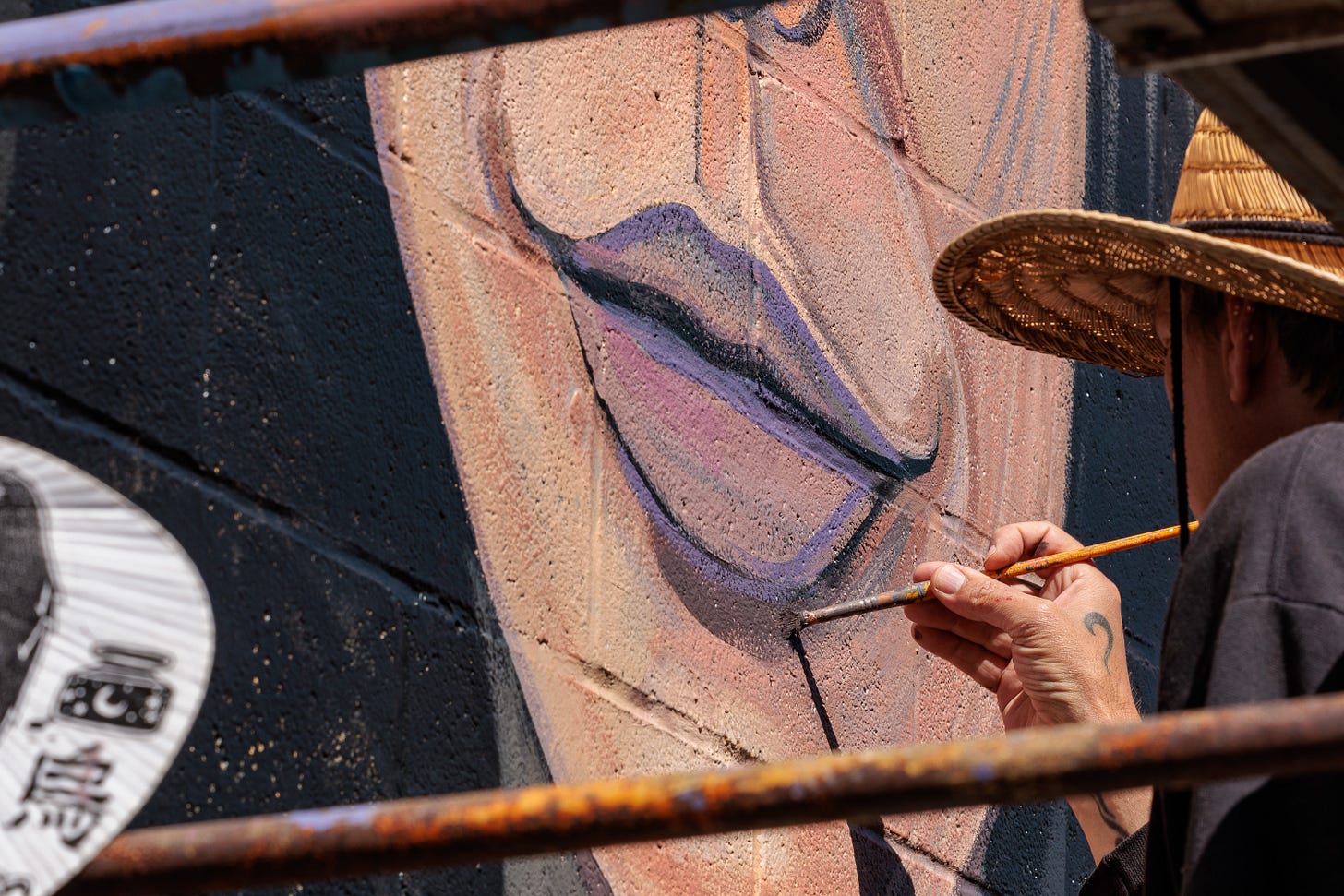 A close-up of Pierre Nagley's hand painting fine details on a face's lips, straw hat visible at the edge of the frame.