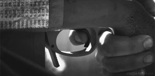 a black and white photo of a man with a beard looking through a sniper rifle .