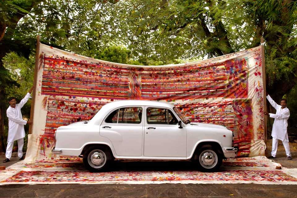 Indian Ambassador car in front of a block printed fabric hold by two men in white kurta
