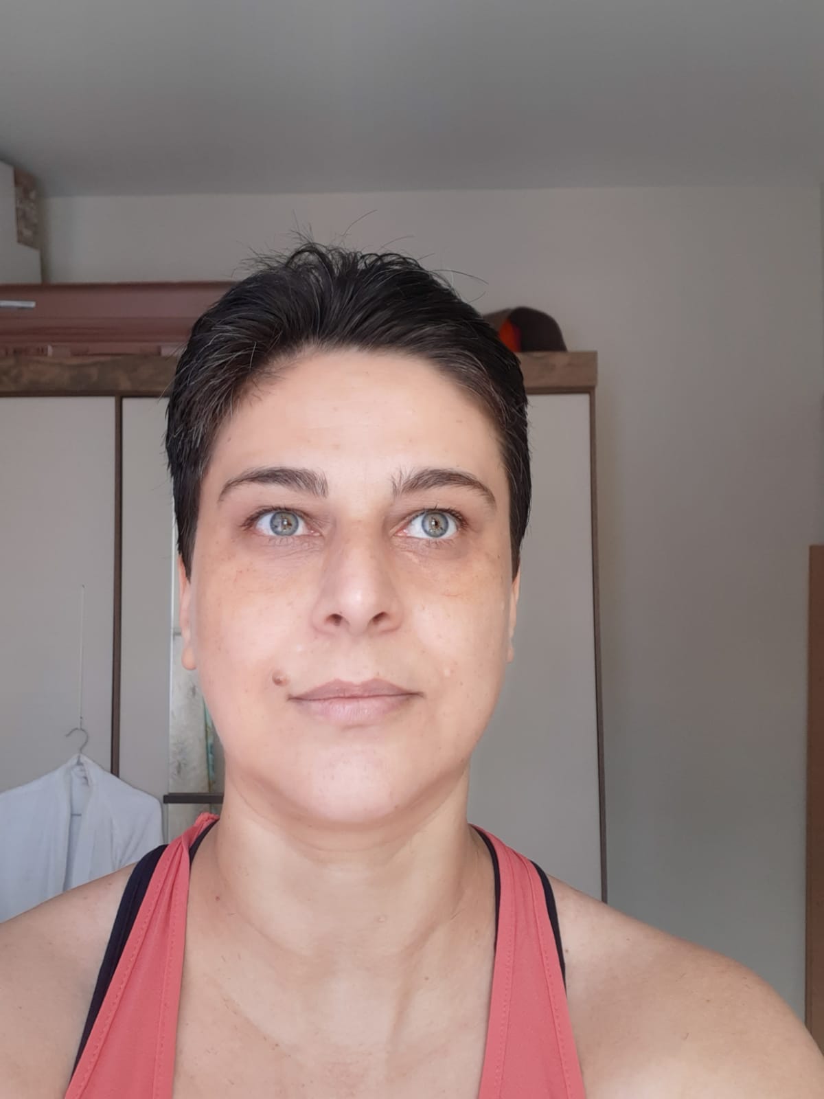 Retrato de Oryanna Borges, uma mulher de pele clara e olhos verdes, com cabelo curto estilo pixie escuro. Ela olha para o horizonte com expressão firme, vestindo uma regata coral.