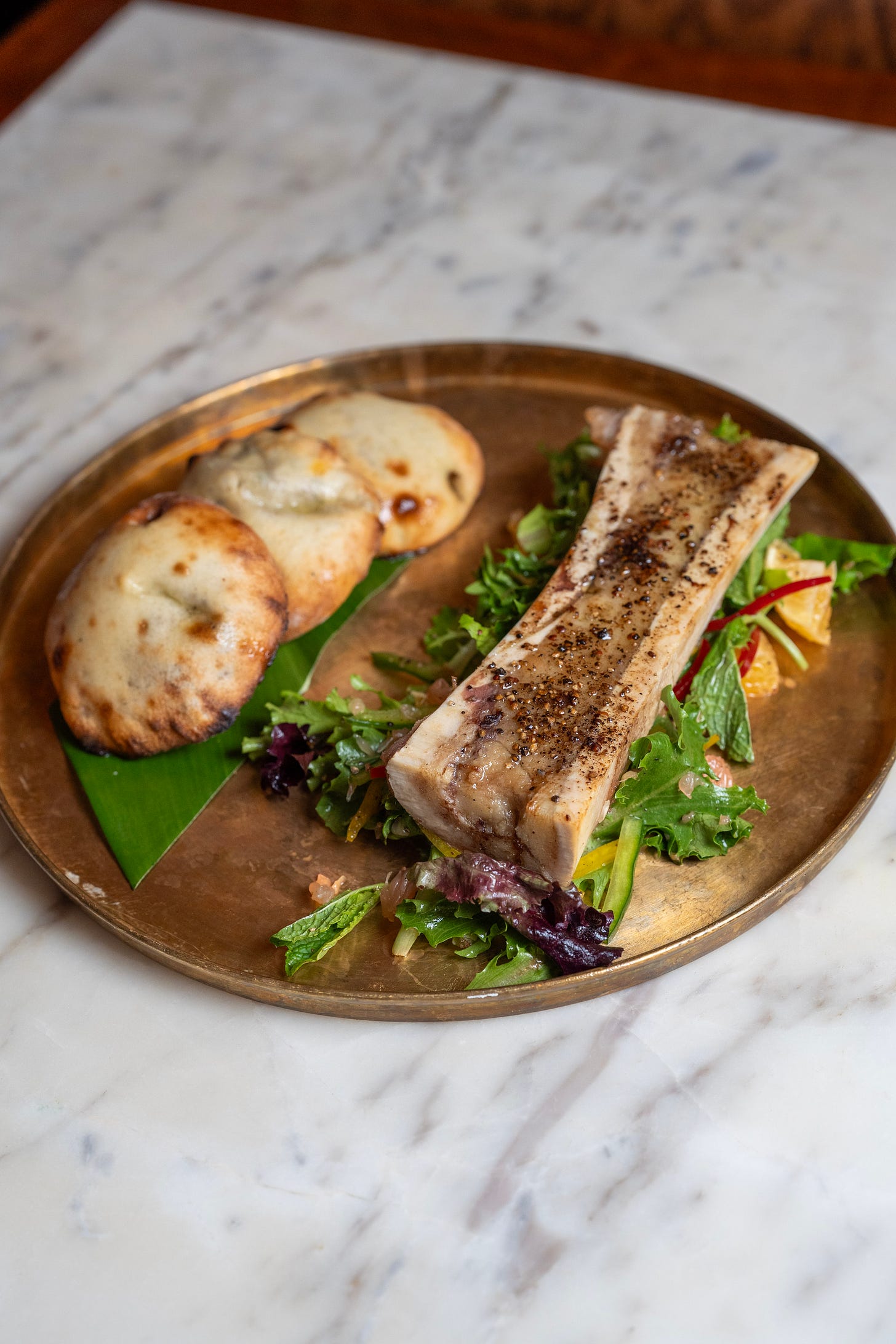 1/2 marrow bone and 3 white dumplings on a gold plate on a marble counter