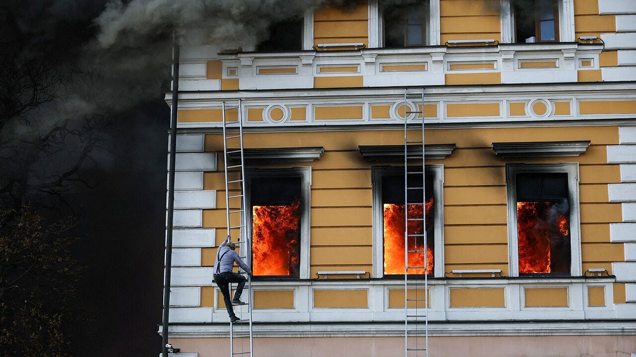 A man climbs down a ladder as flames rise from an administrative building hit by a drone strike, in Kyiv, Ukraine
