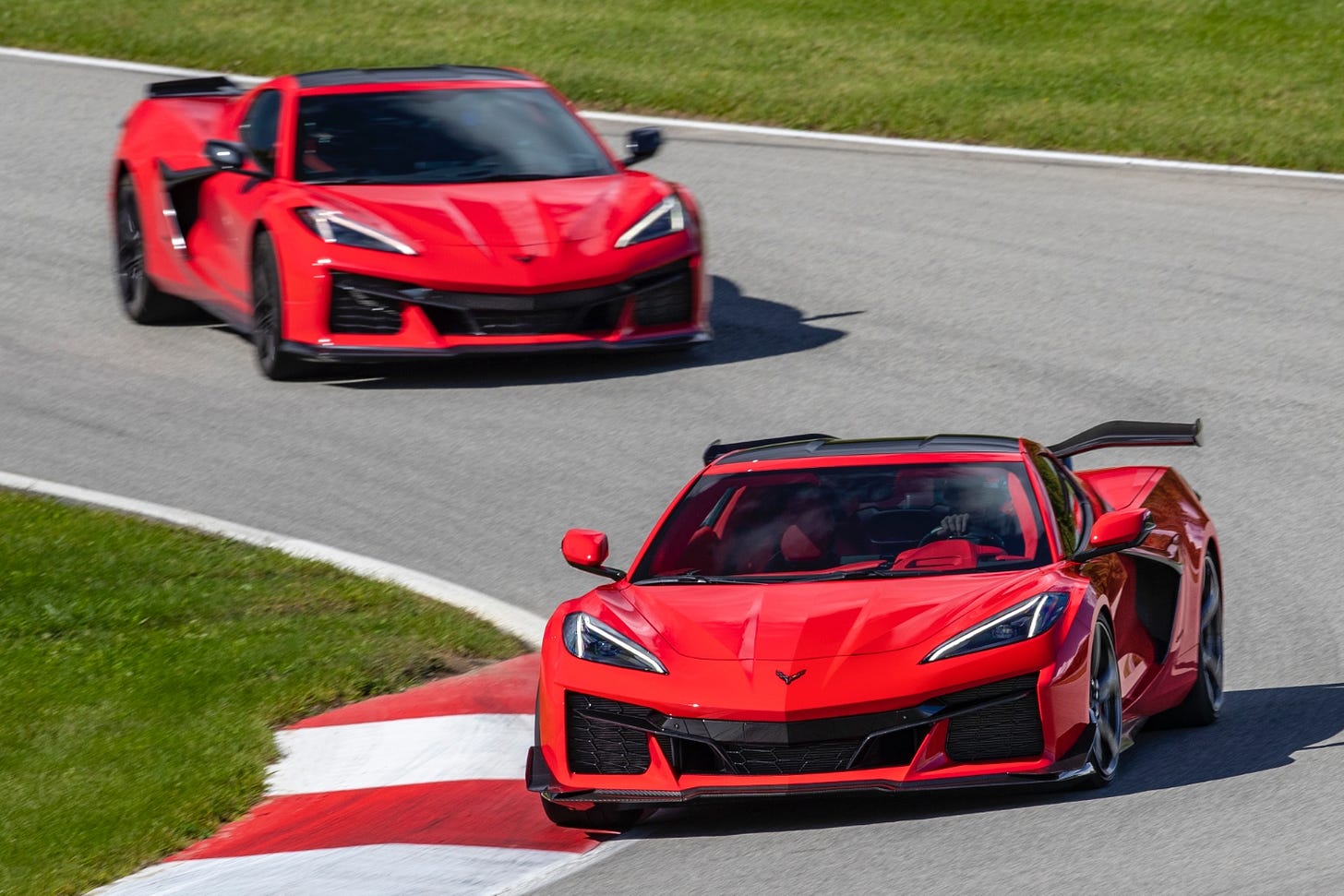 Red Chevy Corvette Z06 models driving through a corner on a race track.