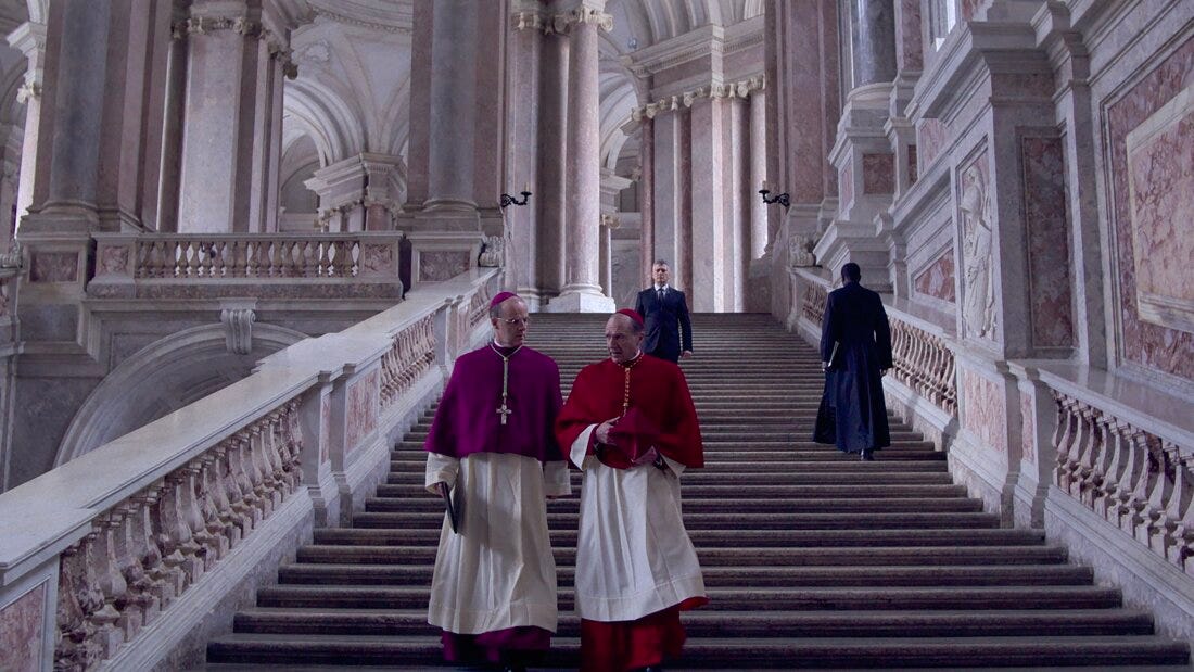 Cardinal O'Malley (Brían F. O'Byrne) confers with Cardinal Lawrence in Conclave. 