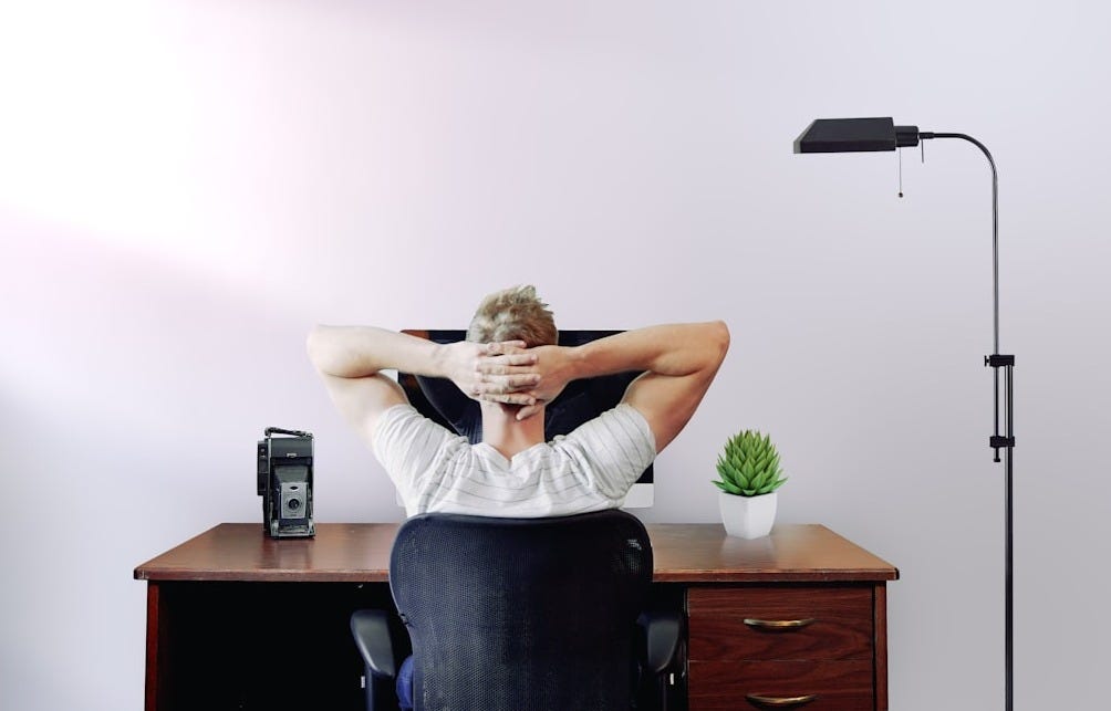 man holding his head while sitting on chair near computer desk man holding his head while sitting on chair near computer desk