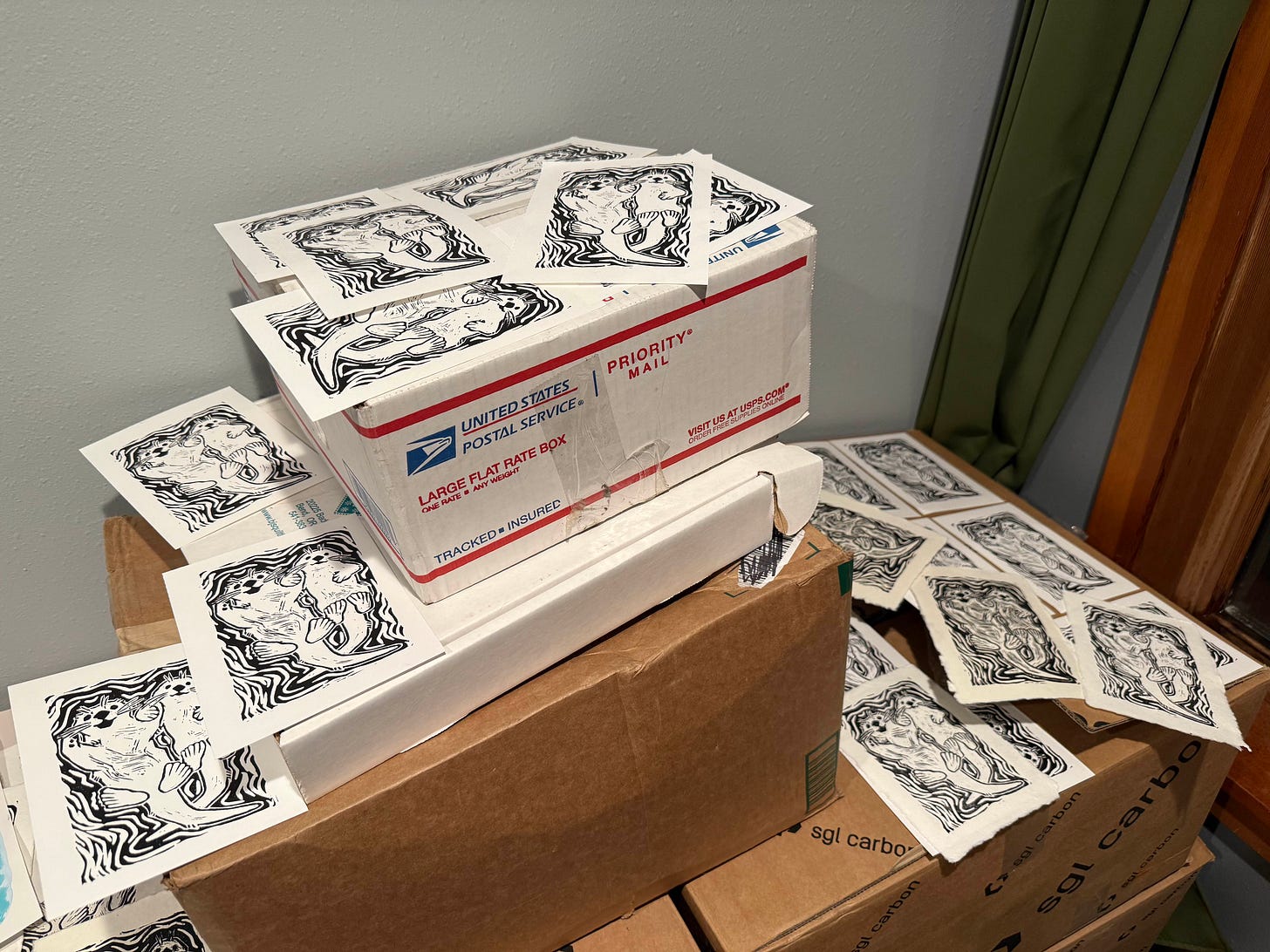 Prints of two otters holding hands laid out to dry on top of moving and shipping boxes.