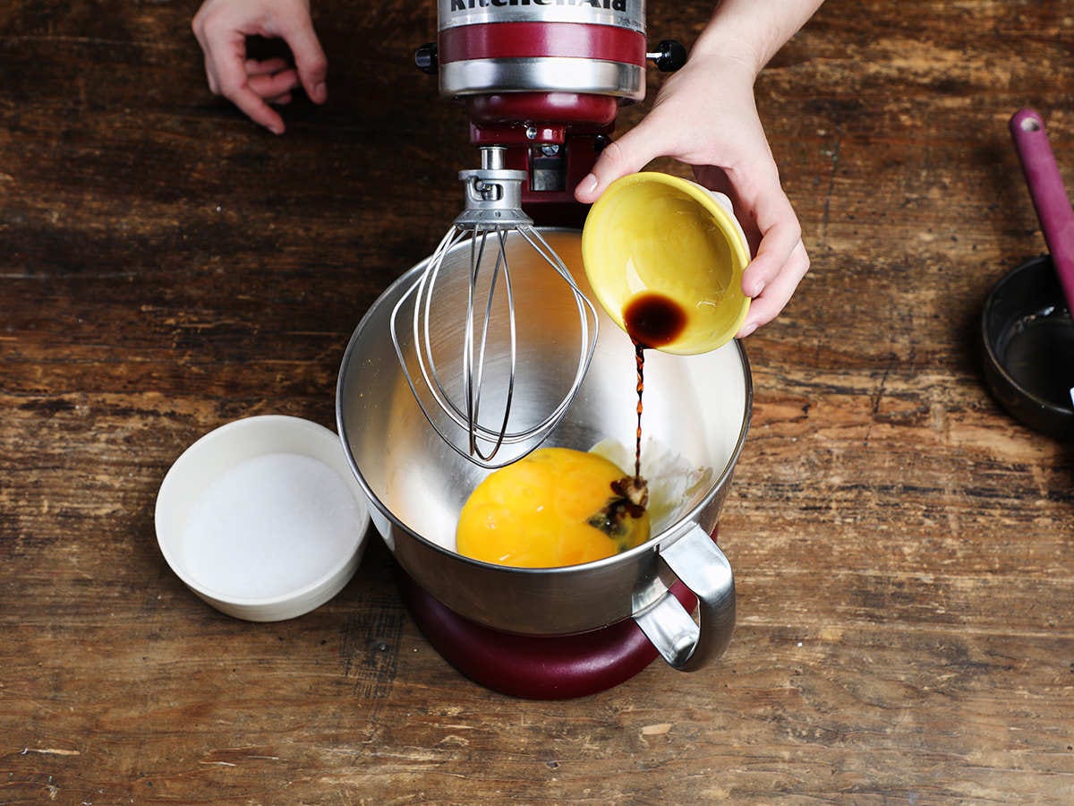 Pouring vanilla into bowl of stand mixer with eggs 