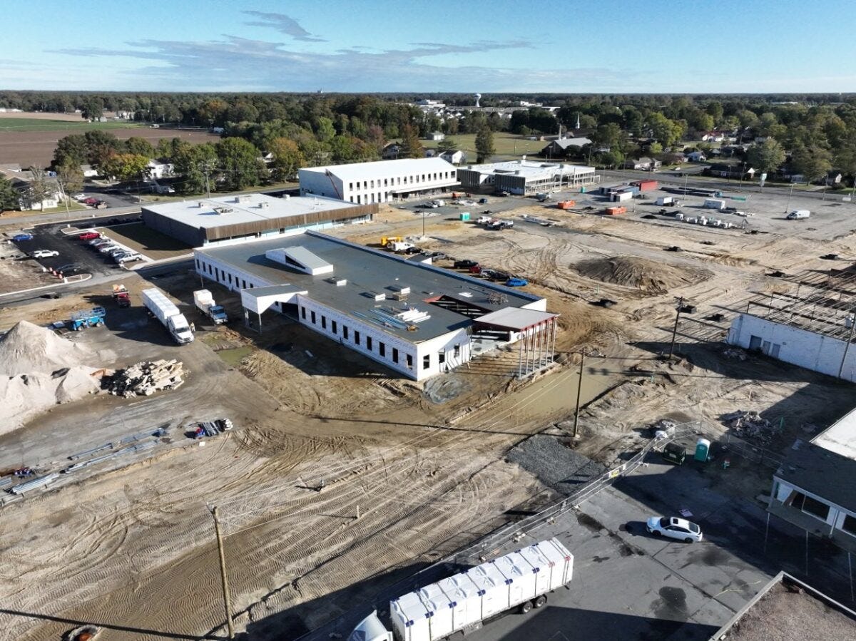 Aerial view of a construction site with partially built structures, construction vehicles, equipment, and dirt piles under a clear sky.
