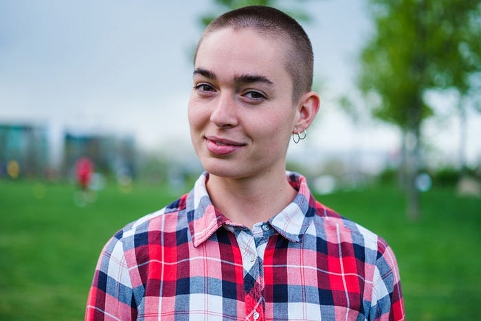 A nonbinary teen with a shaved head in a plaid shirt