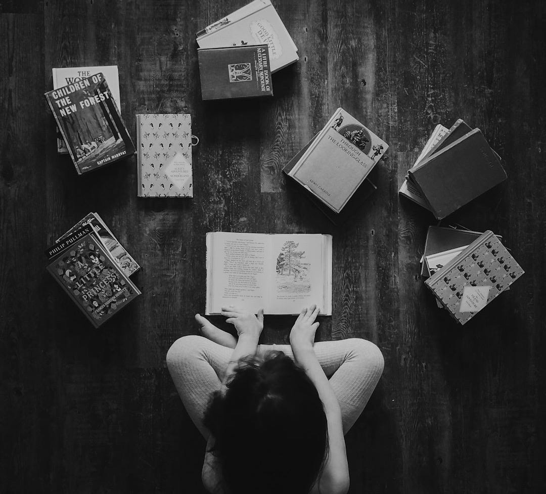 flat lay photography of woman sitting on brown wooden parquet flooring surrounded by books